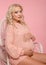 Beautiful pretty pregnant woman expecting maternity hugging her belly. Blonde in knit sweater isolated on studio pink background.