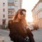 Beautiful pretty young hipster woman in trendy clothes in retro style in fashionable dark sunglasses is posing outdoors