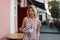 Beautiful pretty young woman with a cute smile in a pink stylish dress with stripes stands near a vintage building