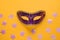 Beautiful purple carnival mask and confetti on orange background, top view