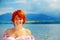 Beautiful radiant girl with red hair and colorful sommer dress beside a lake.
