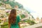 Beautiful rear view of a romantic sweet woman in green dress looking at Positano village from a terrace, Amalfi Coast, Italy