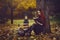 Beautiful red-haired girl with books and a lantern sitting under a tree in the autumn fairy forest. A fabulous autumn