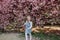 Beautiful red-haired girl sincerely smiles in the park near the sakura. Girl on a spring city street with blooming pink Japanese