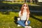 Beautiful red-haired girl sitting on the lawn. In the hands of the girl a glass of coffee. The young lady is warming the morning