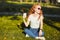 Beautiful red-haired girl sitting on the lawn. In the hands of the girl a glass of coffee. The young lady is warming the morning