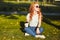 Beautiful red-haired girl sitting on the lawn. In the hands of the girl a glass of coffee. The young lady is warming the morning