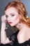 A beautiful red-haired girl with wavy hair, makeup, bare shoulders and long earrings posing on a gray background in the