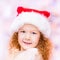 Beautiful red-haired little girl with long curly hair wearing Santa Claus Christmas hat