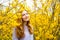 Beautiful red-haired young woman standing near blooming Forsythia bushes in spring garden