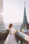 Beautiful red-head bride posing with bouquet on old castle balcony, cityscape background