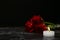 Beautiful red roses and candle on table against black background.