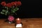 Beautiful red roses in vase with pink bow and red candle on wooden table on dark background