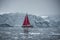 Beautiful red sailboat in the arctic next to a massive iceberg showing the scale. Cruising among floating icebergs in