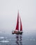 Beautiful red sailboat in the arctic next to a massive iceberg showing the scale. Cruising among floating icebergs in