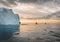 Beautiful red sailboat in the arctic next to a massive iceberg showing the scale. Cruising among floating icebergs in