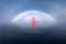 Beautiful red sailboat under a glowing fog bow.