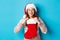 Beautiful redhead girl in santa hat open Christmas stocking and looking surprised, receiving xmas gift, standing over