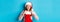 Beautiful redhead girl in santa hat open Christmas stocking and looking surprised, receiving xmas gift, standing over