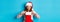 Beautiful redhead girl in santa hat open Christmas stocking and looking surprised, receiving xmas gift, standing over