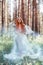 Beautiful redhead woman forest nymph in a blue transparent light dress in the woods spinning in dance. Red hair girls. Art fashion