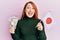 Beautiful redhead woman holding 5000 japanese yen banknotes and japan flag celebrating crazy and amazed for success with open eyes