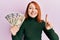 Beautiful redhead woman holding japanese yen banknotes smiling with an idea or question pointing finger with happy face, number