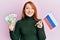 Beautiful redhead woman holding russian ruble banknotes and russia flag smiling with a happy and cool smile on face