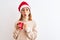 Beautiful redhead woman wearing christmas hat drinking a cup of coffee over  background scared in shock with a surprise