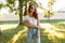 Beautiful redhead young hipster woman in vintage blue jeans in a white t-shirt in trendy sunglasses stands in a park