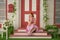 Beautiful redheaded pin up girl in pink polka dot dress and vintage stockings posing near the entrance of her home