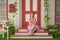 Beautiful redheaded pin up girl in pink polka dot dress and vintage stockings posing near the entrance of her home