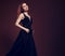 Beautiful redheaded young model with bright foxy hair posing in fashion chic black dress with long skirt on studio grey background