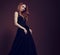 Beautiful redheaded young model with bright foxy hair posing in fashion chic black dress with long skirt on studio grey background