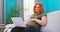 Beautiful redheaded young woman sits on living room couch with laptop in lap, clutching her