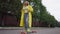 Beautiful relaxed retro woman putting on yellow rain coat standing with skateboard outdoors on street road. Wide shot