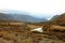 A beautiful river flowing through an autumnal valley surrounded by mountains under low clouds