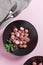 Beautiful roasted radishes in a black plate on pink table close up