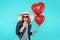 Beautiful rocker girl in leather jacket and summer hat kissing heart shaped lollipop and holding heart shaped balloons.