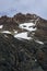 Beautiful rocky mountain peaks with veins of orange minerals, snow patches, and blue sky with wispy white clouds