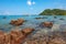 Beautiful rocky stones in the turquoise sea and a pier with speed boats and tourists in the distance.