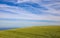 Beautiful rolling green hill against blue sky covered with Cirrus clouds and the blue Ocea