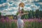 Beautiful romantic girl in a delicate dress with a hat sits in a flower field of purple lupine flowers. Soft selective focus