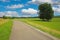 Beautiful rural countryside idyllic belgian landscape, vibrant strong green meadows, trees, bike cycle path, blue summer sky -