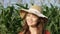 A beautiful rural girl under shade of an elegant straw hat in the green field of corn. Photo of a happy country female