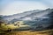 Beautiful rural mountain landscape in the morning light with fog, old houses and haystacks