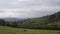 Beautiful rural mountain landscape with a village on the hills and a forest. Cloudy sky and mountain peaks in the distance