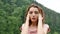 Beautiful sad girl standing in the summer rain against the backdrop of mountains covered with forests. Young unhappy