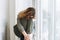 Beautiful sad unhappy teenager girl with curly hair in close pose sitting on the window sill