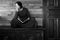 A beautiful sad woman sits with a book on an old black chest on a wooden background